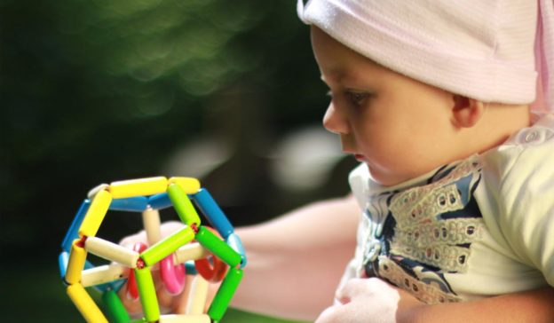 Bébé portant un chapeau rose, tenant joyeusement un jouet sûr bébé coloré à l'extérieur.
