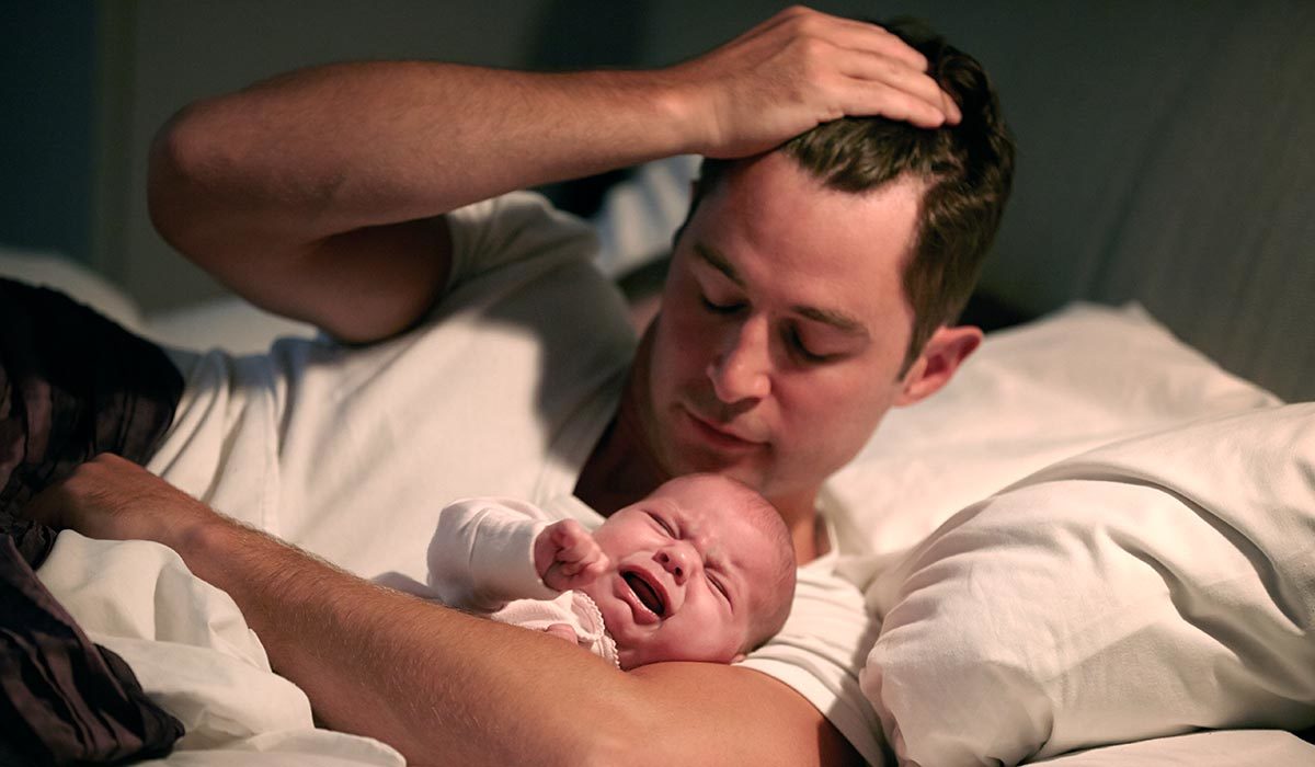 Un homme est au lit, apaisant un bébé qui pleure dans ses bras, espérant des moments de bébés endormis.