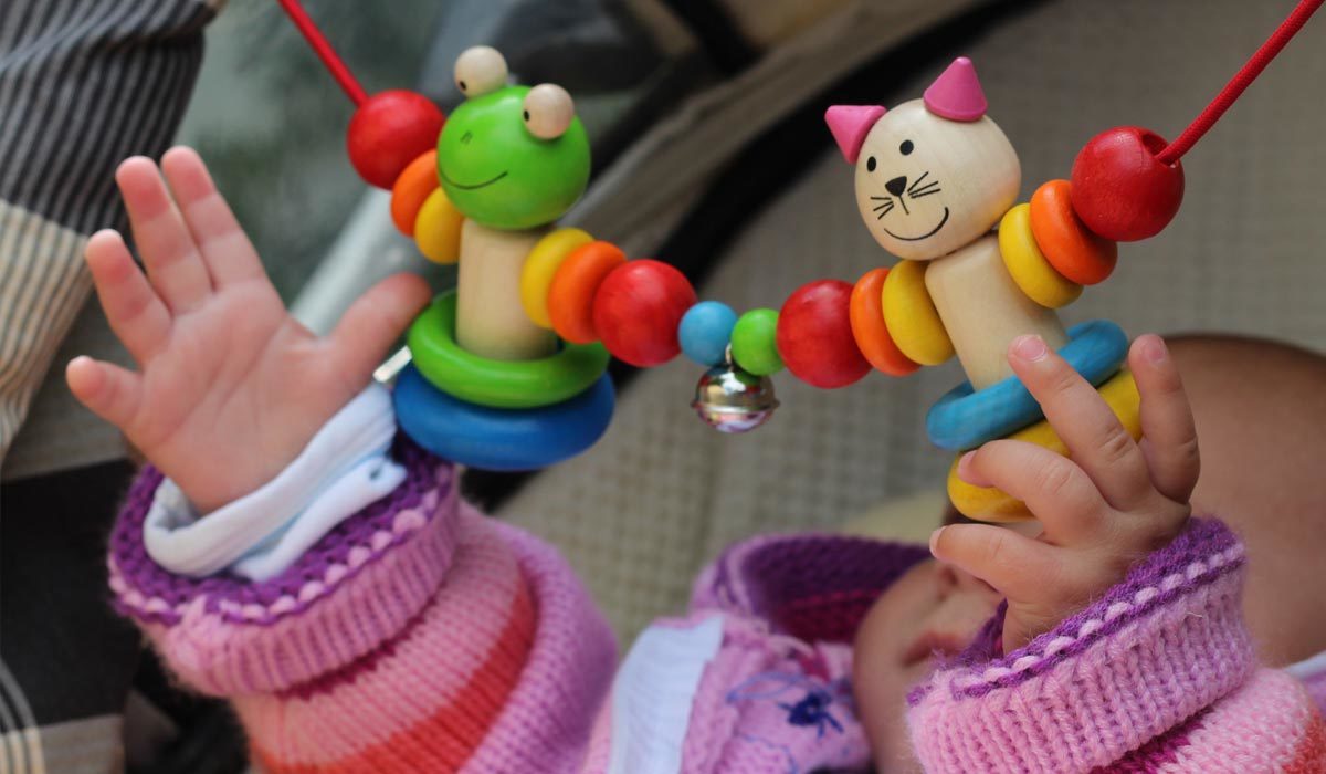 Bébé attrape un jouet coloré avec des figurines d'animaux dans une poussette tout en se déplaçant avec bébé dans un pull rose.