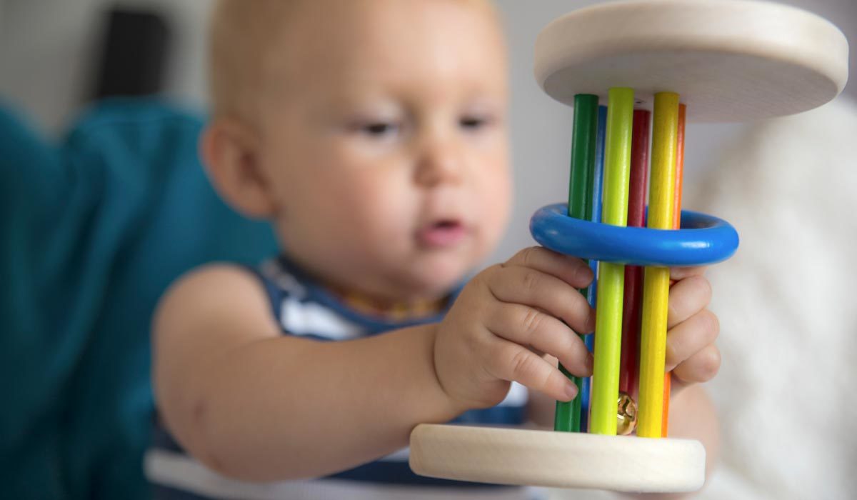 Bébé apprend à jouer avec un hochet en bois coloré sur un canapé bleu.