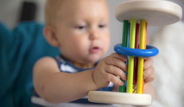 Bébé apprend à jouer avec un hochet en bois coloré sur un canapé bleu.