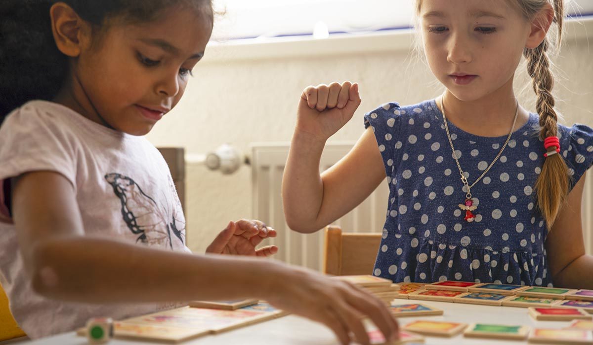 Deux jeunes filles, profondément liées par l'amitié, jouent à un jeu de société à table, concentrées et engagées.