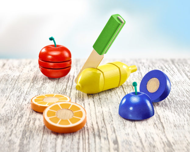 Fruits jouets en bois avec velcro, comprenant une pomme, une orange et une banane, sur une surface en bois clair.